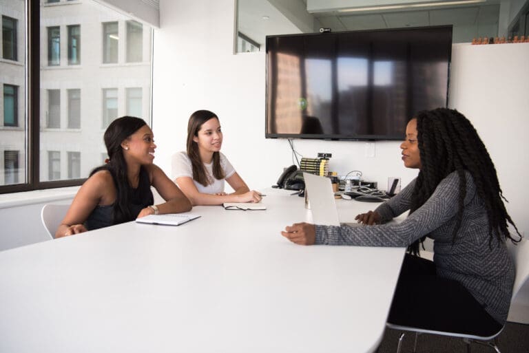 Three women sitting around a table in a professional setting. Human Resources and Operations Manager.